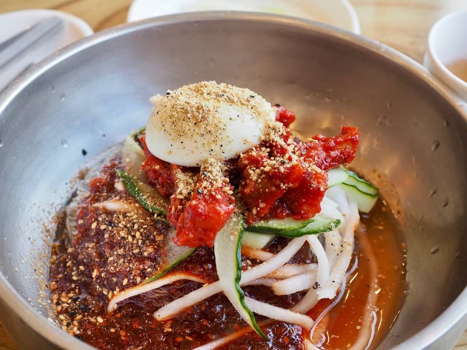 A bowl of mul naengmyeon with buckwheat noodles, sliced cucumber, boiled egg, and icy broth served at a naengmyeon restaurant in Seoul