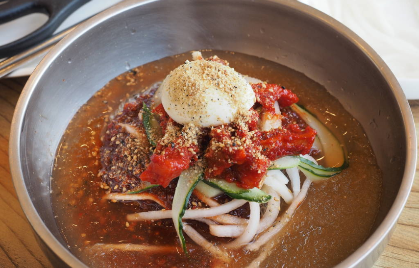 A bowl of mul naengmyeon with buckwheat noodles, sliced cucumber, boiled egg, and icy broth served at a naengmyeon restaurant in Seoul